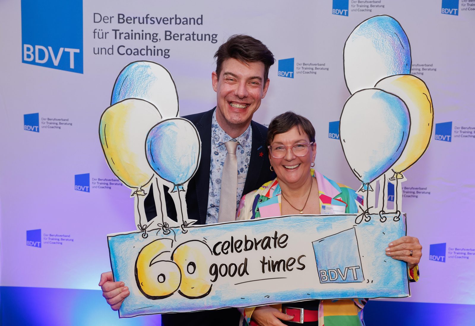 Timothy Tasch und Tanja Hartwig feiern mit einem Schild „60 – celebrate good times“ das BDVT-Jubiläum