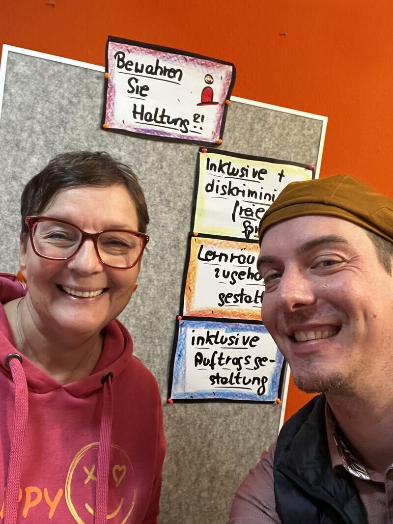 Tanja Hartwig und Timothy Tasch vor einer Pinnwand mit den Kernpunkten des Vortrags: Bewahren Sie Haltung, inklusive Sprache, Lernräume zugänglich gestalten, inklusive Auftragsgestaltung